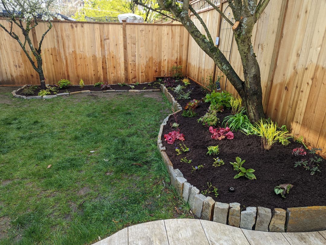 Garden landscape with flower beds, fresh plants, and wooden fencing in a serene backyard.