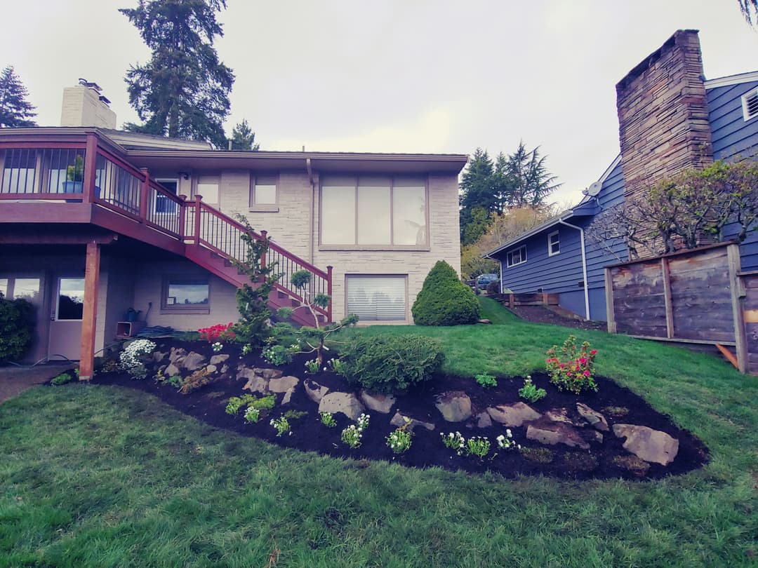 Landscaped backyard with flower beds, grass, and a two-story house in a tranquil setting.