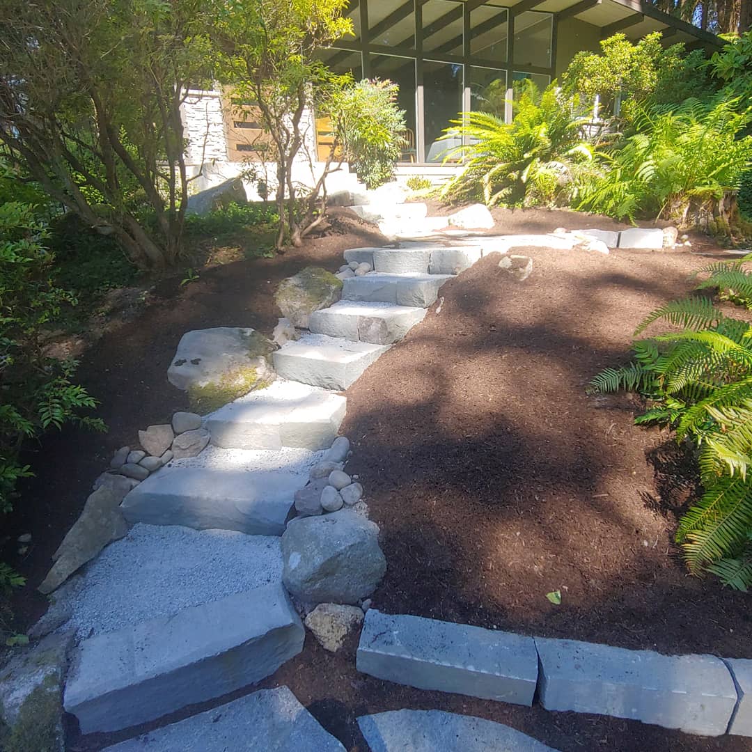 Stone pathway leading to a modern home, surrounded by lush greenery and landscaping.