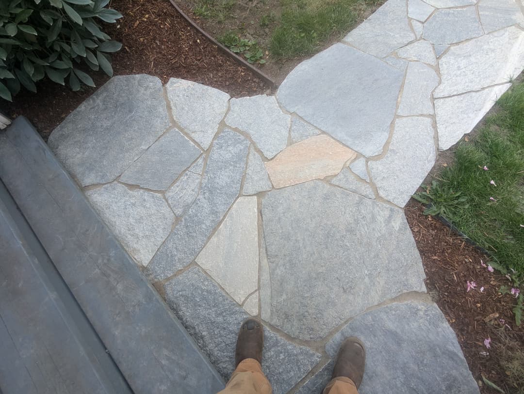 Stone pathway with irregular slate tiles and garden edge, viewed from above.