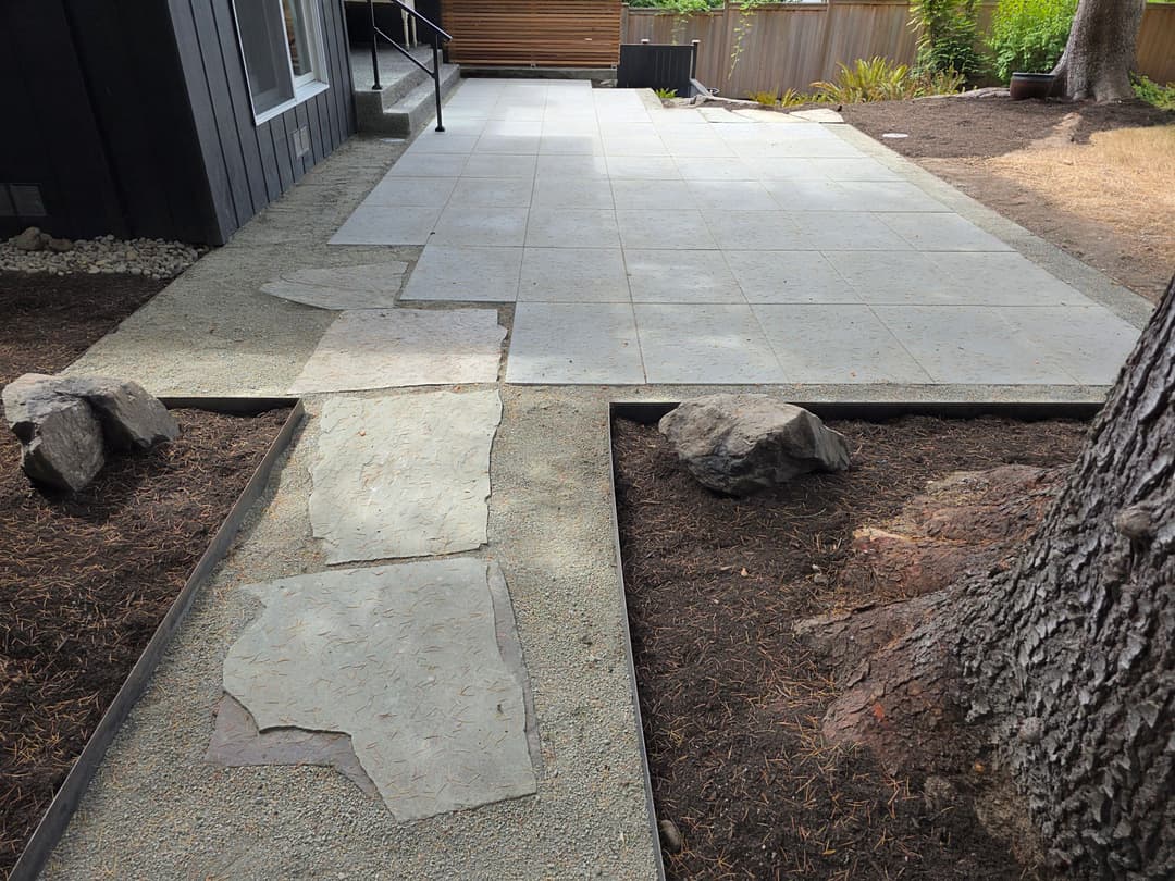 Modern outdoor patio with stone pathway and landscaped borders, featuring gray concrete slabs.