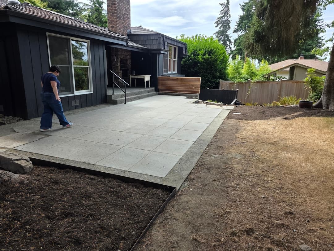Person walking on a modern concrete patio in a residential backyard setting.