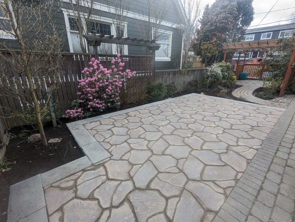 Stone patio layout with pink flowers, garden greenery, and a cozy outdoor setting.