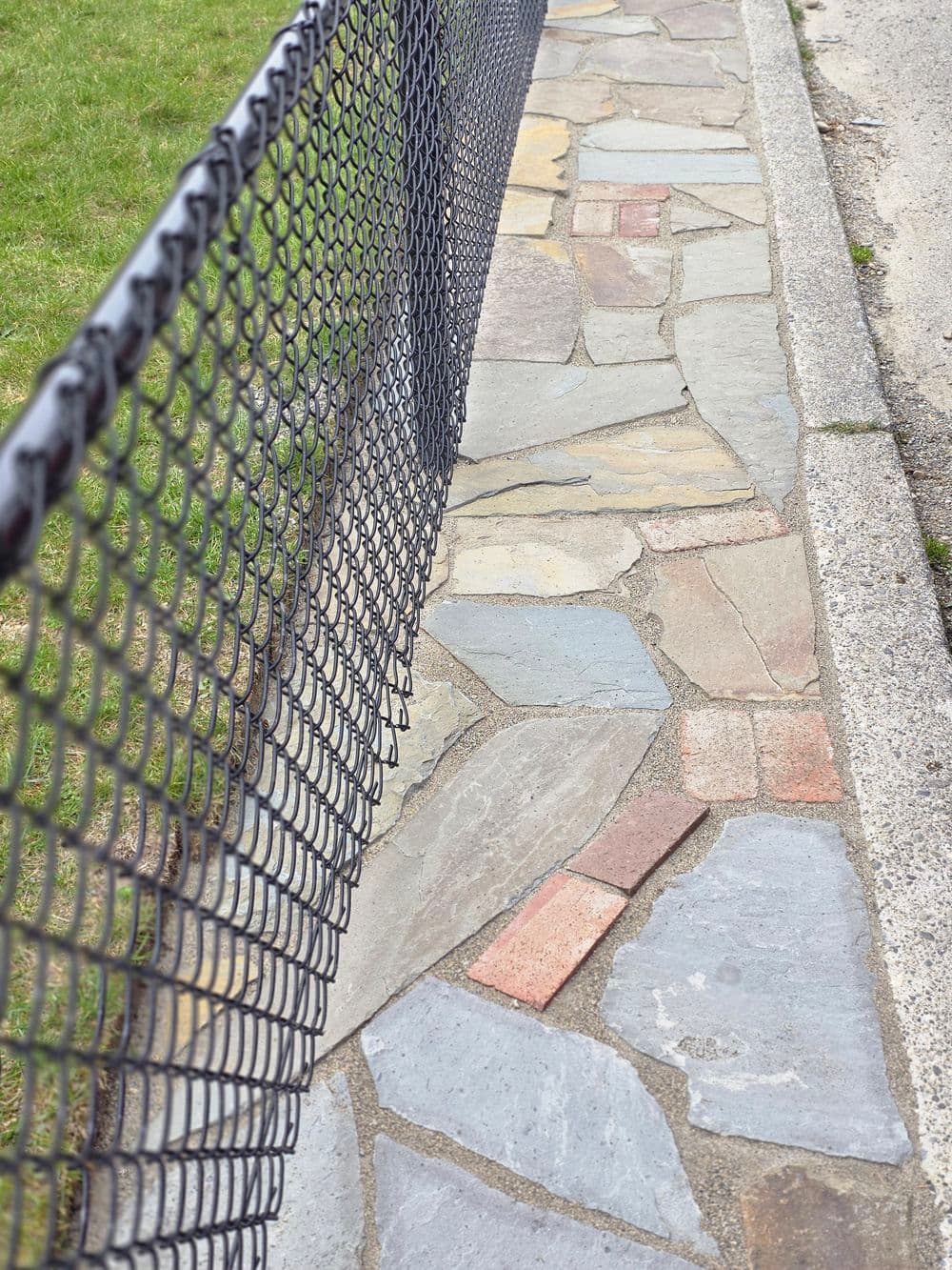 Stone path beside black chain-link fence in grassy area. Ideal for outdoor landscaping.